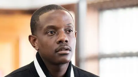 Gallo Images via Getty Images Close-up of Bellarmine Mugabe. The partial black and white collar and black shoulders of his jacket can be seen. He is standing indoors.