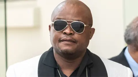 Gallo Images via Getty Images Brown Mogotsi, wearing shades, a black top and white jacket with a black collar and trim pictured in Cape Town on 24 February 2026.