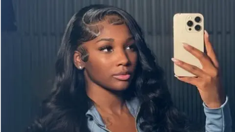 Ashlee Jenae / Instagram Ashly Robinson in a blue top, holding a phone as she takes a selfie of herself