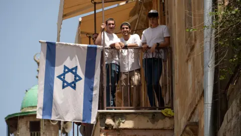 A group of Israeli settlers stand in a balcony with an Israeli flag in Jerusalem's Old City.