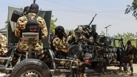 AFP via Getty Images Nigerian soldiers seated in trucks, wearing military camouflage uniform and wearing black hood
