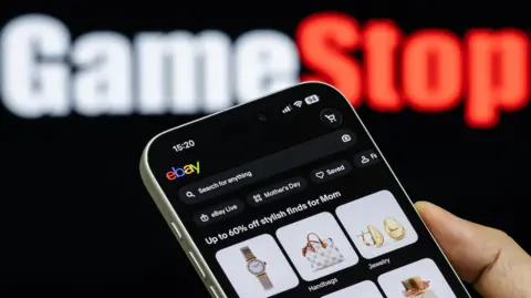 Getty Images eBay on a phone in the foreground with the GameStop logo in the background.