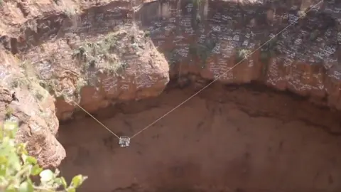 Yemen civil defence Two wires with a cage on them stretch the length of a volcanic crater during a rescue mission to retrieve the body of a free-climber.