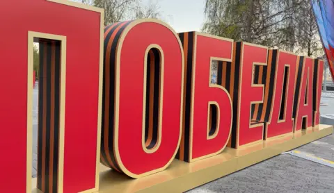A sign near Red Square reads 'Pobeda!' meaning 'Victory!' in Russian, in large red letters.