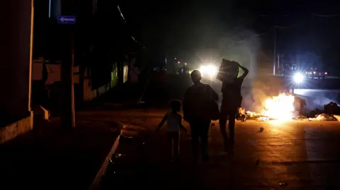 Reuters Three children stand before a burning pile of rubbish in the middle of a road in Havana, the street is completely unlit barring distant car headlights. 