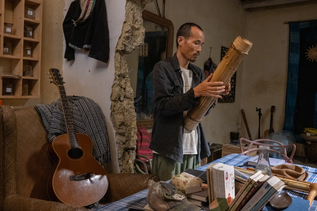 岜農手持一把他回到廣西農村老家後學習的傳統樂器。他在廣州居住期間自學了吉他。