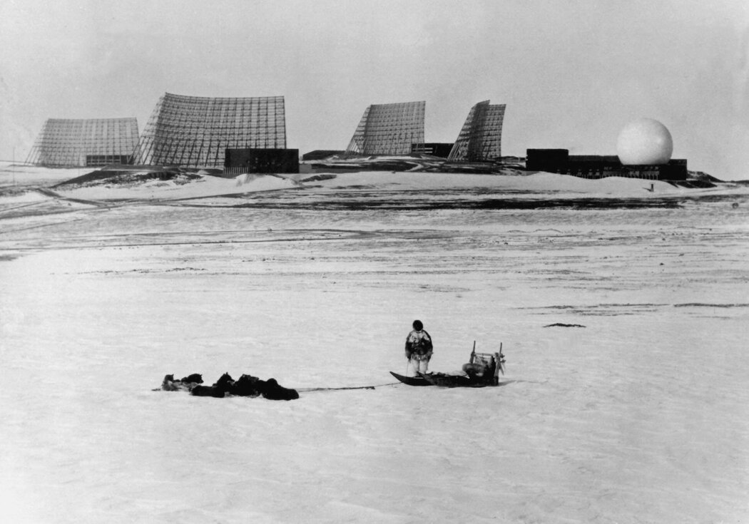 1966年，格陵蘭島北部，一名當地人帶著他的狗拉雪橇，凝望著美國人建造的圖勒空軍基地。