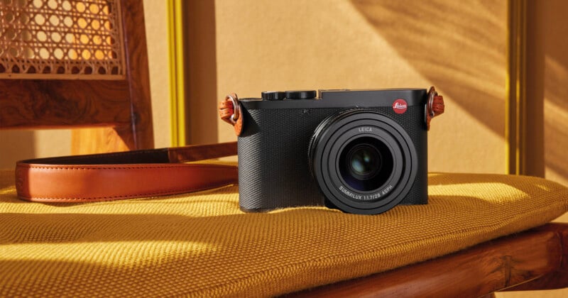 A black Leica camera with a leather strap sits on a textured yellow cushion next to a wooden chair.