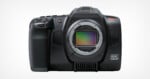 A high-resolution, black digital camera with a visible lens mount and a textured grip on the left side. The camera body shows 
