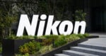 A large, white, three-dimensional Nikon logo stands in a garden bed next to a set of concrete stairs.