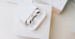 A pair of white wireless earbuds with black accents sit in an open charging case, placed on a white box against a light background.