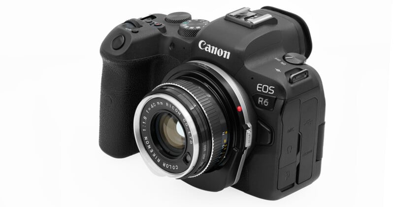 A black Canon EOS R6 digital camera with a manual focus lens attached, viewed from an angle showing the lens, grip, and top controls.