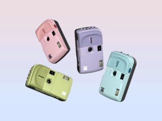 Four Kodak cameras in pastel pink, purple, green, and blue are floating against a gradient pastel background. Each camera has a retro style, with a prominent flash and lens on the front.