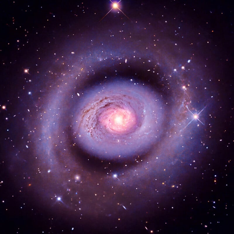 A colorful spiral galaxy with glowing, swirling arms and a bright center, surrounded by numerous stars and cosmic dust against a deep space background.