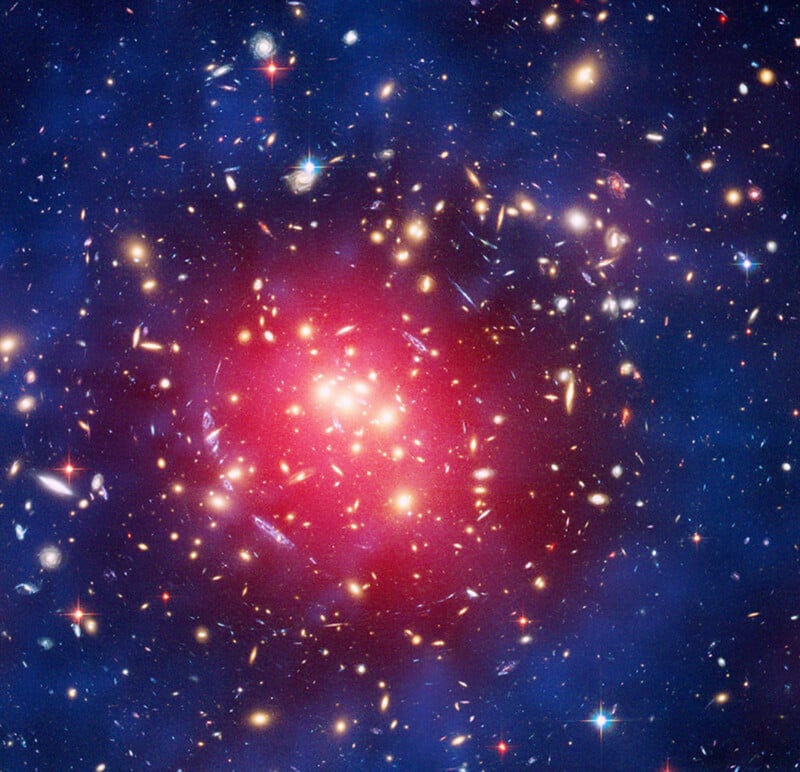 A colorful image of a galaxy cluster, with bright stars and galaxies scattered in a blue and red glowing cloud, showing the vastness and density of space.