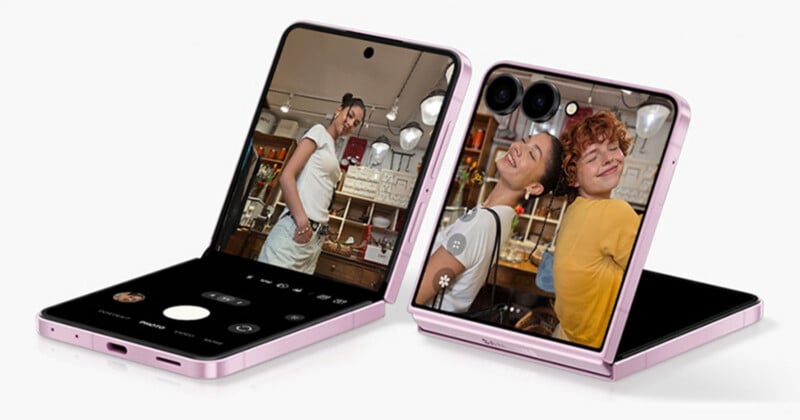 Two pink foldable smartphones, partially open, display a camera app and two people posing playfully for a photo inside a cozy, well-lit room.