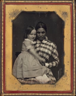 A daguerreotype portrait of a Black woman holding a young white girl on her lap, both looking toward the camera.