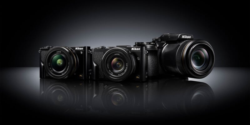 Three Nikon cameras of varying sizes and lens types are displayed side by side on a glossy black surface with a dark, gradient background.