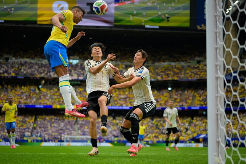 A Brazilian soccer player heads the ball near the goal as two German defenders try to block him. The stadium and fans are visible in the background.