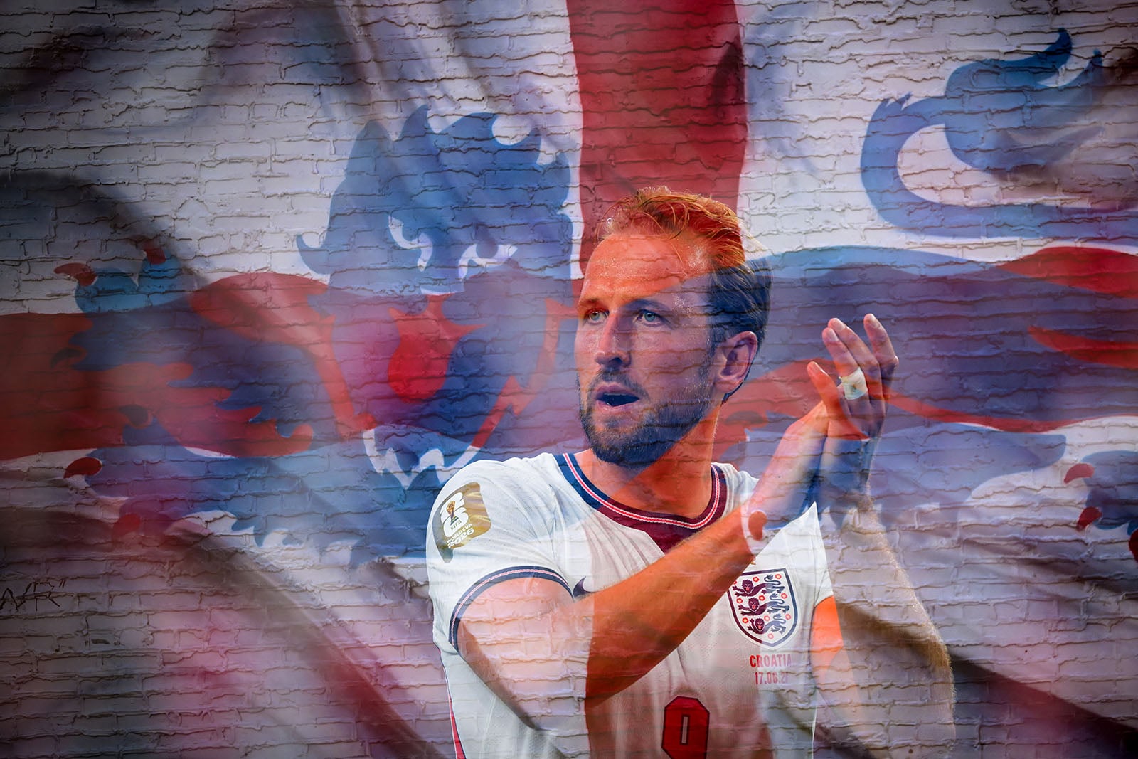 A male England soccer player claps, superimposed over a faded St. George’s Cross flag with a stylized lion, on a textured brick wall background.