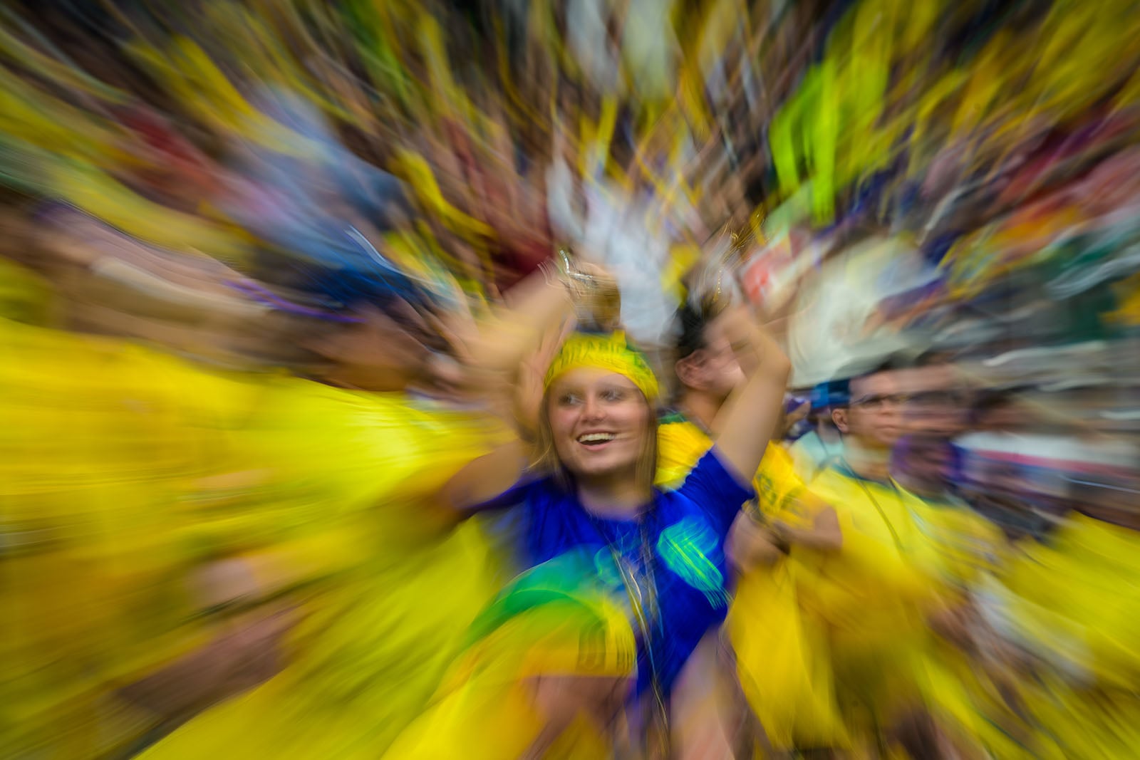 A woman in a blue shirt and yellow headband cheers in a crowd, with a zoom blur effect making the scene dynamic and colorful.