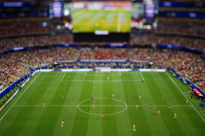 Aerial view of a crowded stadium during a soccer match, with players on a green field and fans filling the seats in the background.