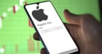 A hand holds a smartphone displaying the Apple Inc. logo and stock info, with 