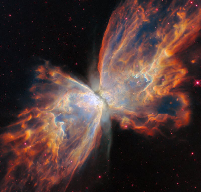 Colorful nebula resembling butterfly wings stretches across space, with bright orange, blue, and pink gas clouds against a black background dotted with small stars.