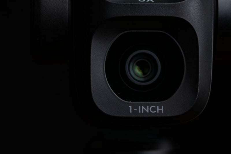 Close-up of a camera lens with the text "1-INCH" printed below the lens, set against a dark background.
