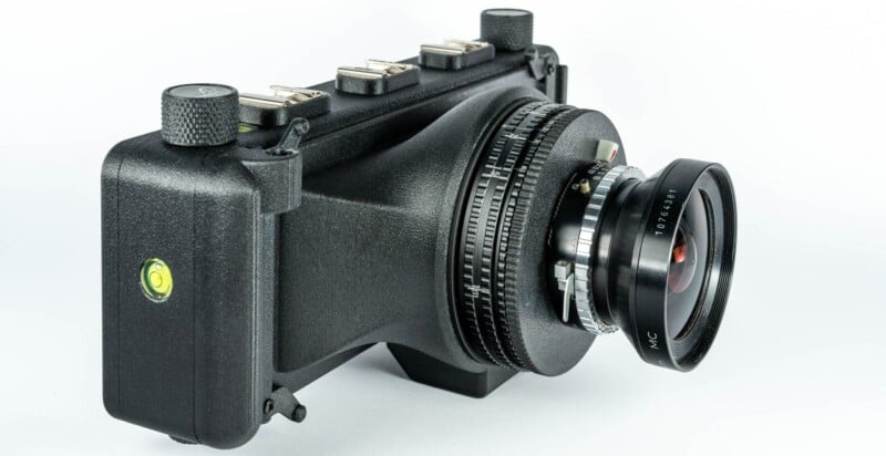 A black, 3D-printed panoramic film camera with a wide-angle lens and a built-in spirit level on the side, viewed from a high angle against a white background.