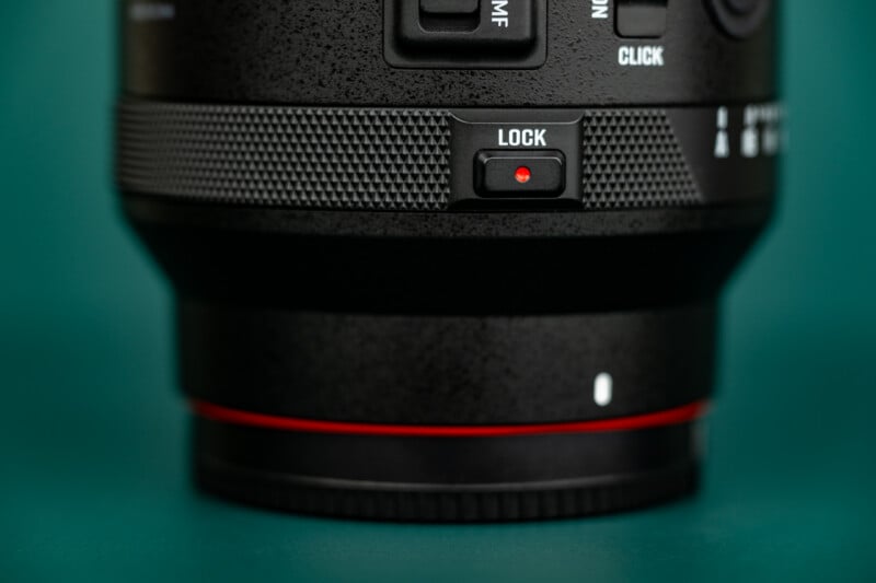 Close-up of a camera lens showing a textured grip, a "LOCK" switch with a red indicator, and part of a red ring near the base against a green background.