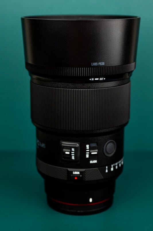 A close-up photo of a black camera lens with various buttons, switches, and markings, set against a solid green background.