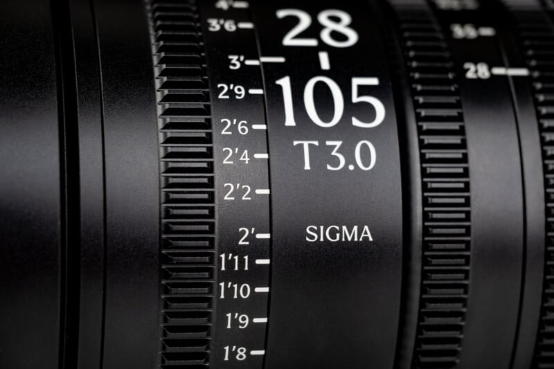 Close-up of a Sigma camera lens showing focus and zoom markings, including 28-105mm focal length and T3.0 aperture, with detailed numbers and textured grip rings visible.