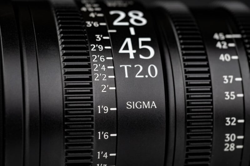 Close-up of a Sigma camera lens showing focal length markings from 28 to 45 and an aperture value of T2.0. The focus and zoom rings have textured grips and detailed white numbering on a black surface.