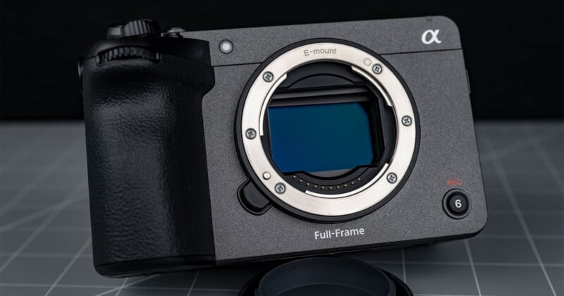 A close-up of a Sony Alpha full-frame mirrorless camera body, without a lens, showing the sensor and E-mount, placed on a gray grid-patterned surface.