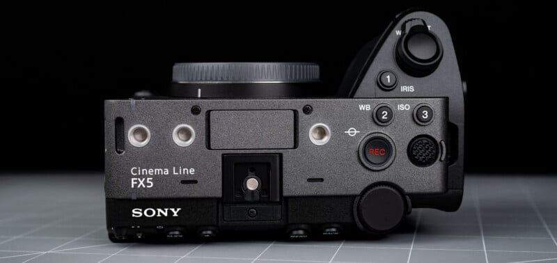 Top view of a Sony Cinema Line FX5 camera body, showing control buttons, dials, REC button, and lens mount, all on a gray grid surface with a black background.