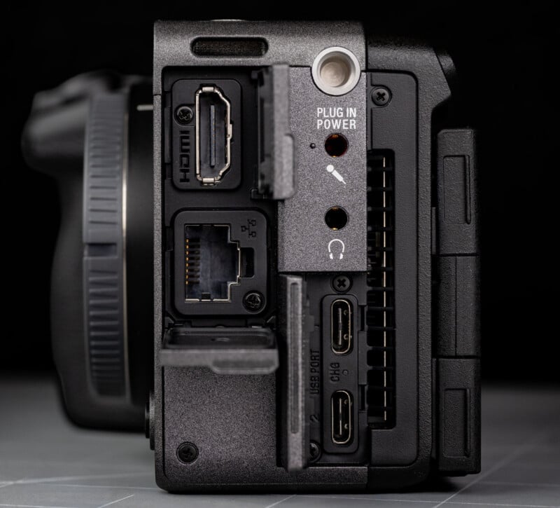 Close-up of a camera's side panel showing various ports: HDMI, LAN, USB-C, headphone and microphone jacks, and a power input. The covers for some ports are open, revealing the connectors.