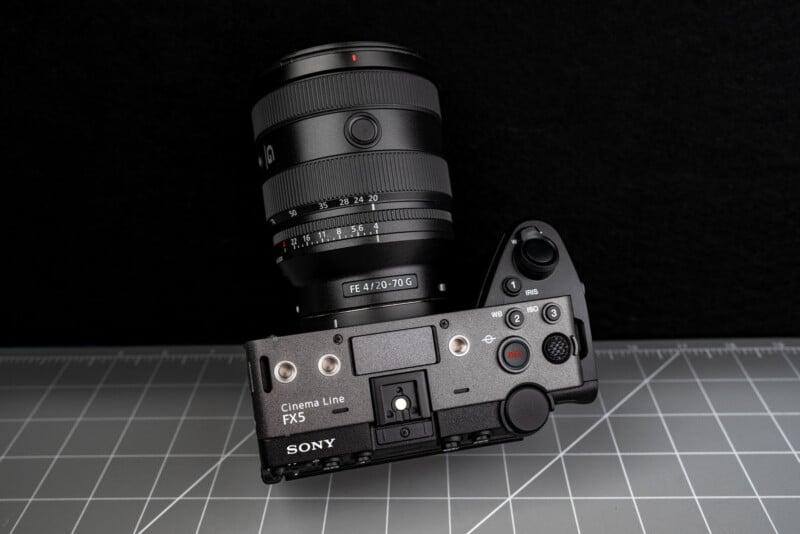 A Sony Cinema Line FX3 camera with a FE 4/20-70 G lens is placed on a gray cutting mat, viewed from above against a black background.