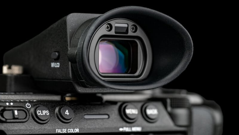 Close-up of a digital camera's electronic viewfinder and control buttons, showing lens reflections and detailed texture on the camera body, against a black background.