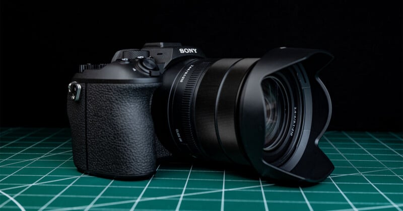 A black Sony digital camera with a wide lens hood is placed on a green cutting mat with grid lines. The background is solid black.
