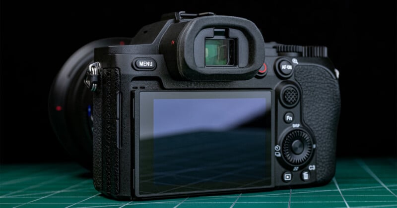 A digital camera with a large LCD screen and various control buttons is placed on a green cutting mat, photographed from the rear.