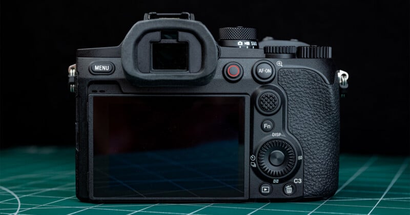 A close-up of the back of a digital camera showing its screen, buttons, and viewfinder, placed on a green cutting mat with a black background.