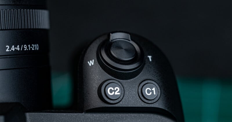 Close-up of a camera body showing a zoom lever labeled W and T, a C2 button, and a C1 button, with part of the lens visible on the left.