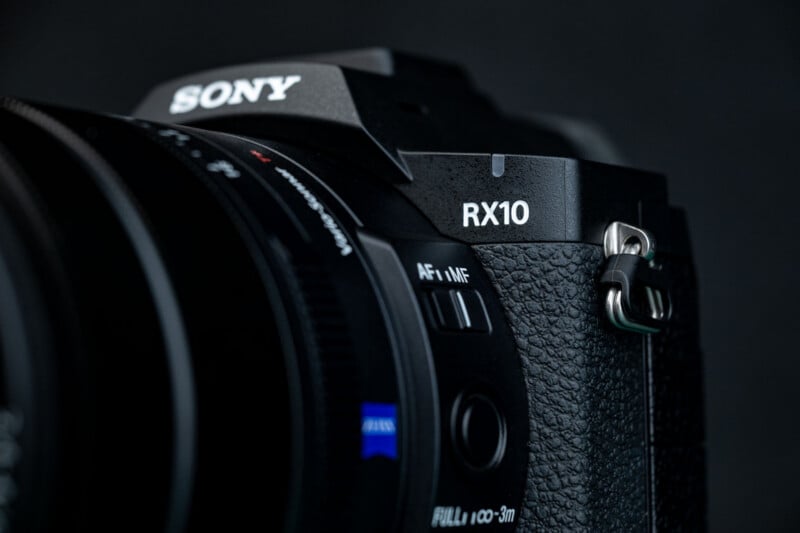 Close-up of a black Sony RX10 camera showing the textured grip, lens, and control switches, with the Sony and RX10 logos clearly visible against a dark background.
