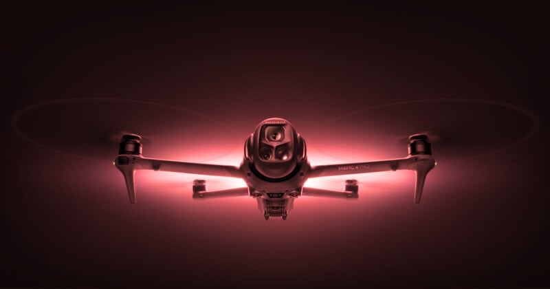 A drone with glowing red lights is captured from the front, highlighting its camera and four propellers against a dark background.