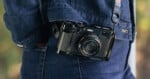 A person wearing a blue denim jacket has a vintage-style black camera hanging from a strap over their shoulder. The camera rests against their side.