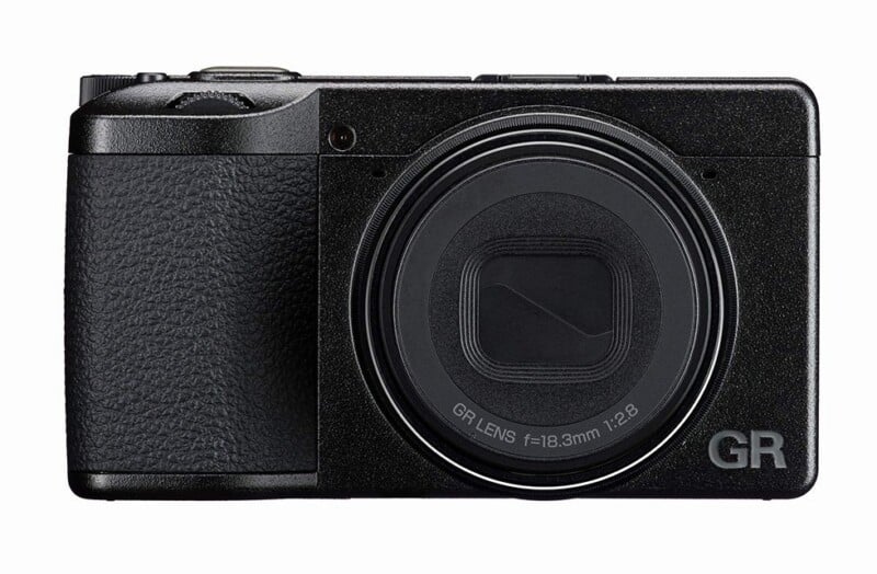 A compact black digital camera with a textured grip and lens cover, labeled "GR LENS f=18.3mm 1:2.8" and "GR" on the lower right corner, shown facing forward against a white background.