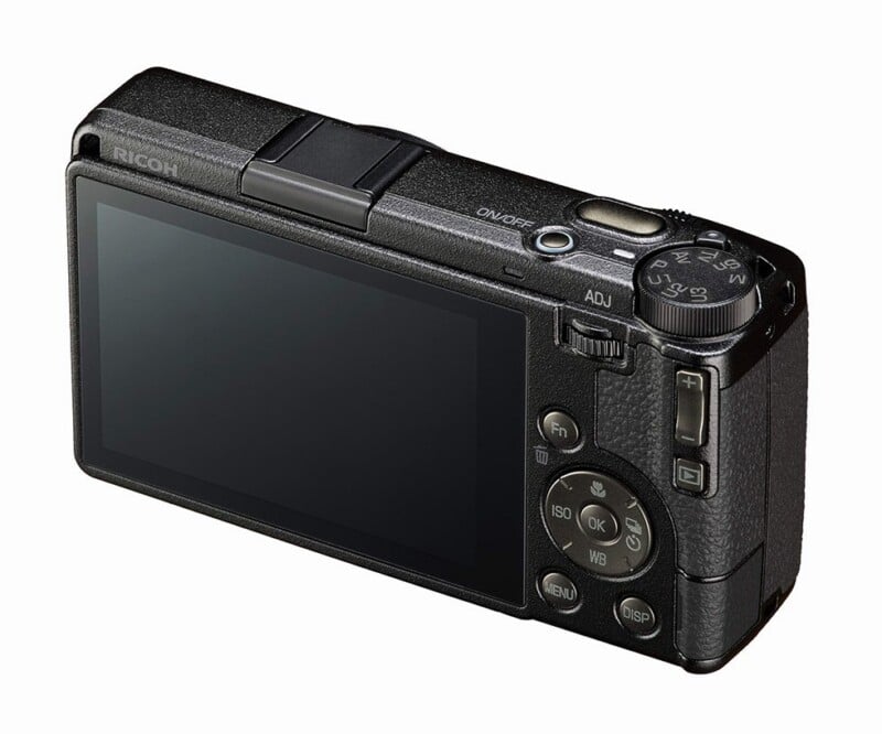 A black Ricoh digital camera shown from the back, displaying its LCD screen, control buttons, and mode dial, isolated on a white background.