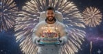 A person in an astronaut suit holds a colorful birthday cake with lit candles. Bright fireworks light up the night sky behind them, creating a festive atmosphere.