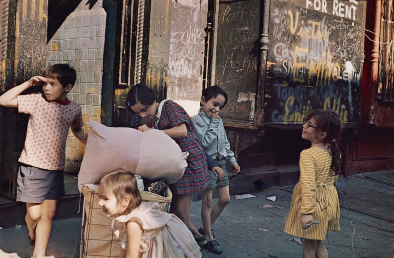 Five children play on a city sidewalk in front of a building with graffiti and a "FOR RENT" sign.